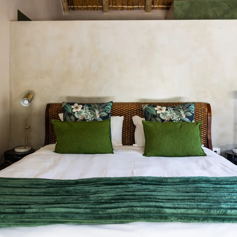 A double bed with green cushions against a plaster wall