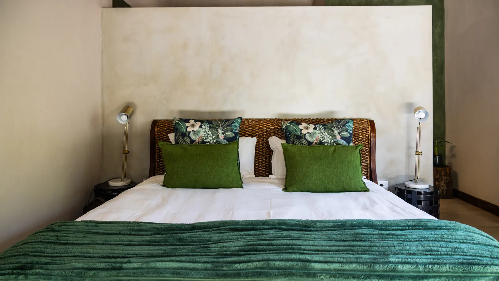 A double bed with green cushions against a plaster wall